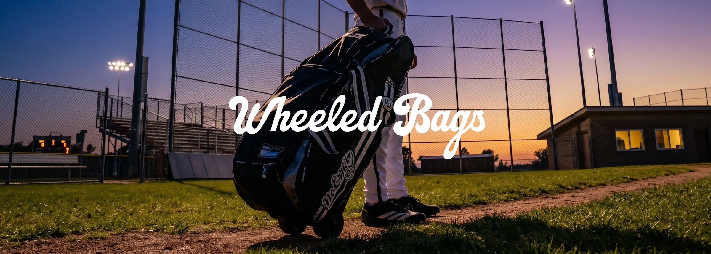 Baseball, softball player rolling a rugged No Errors catcher bag with heavy-duty FatBoy wheels a dirt parking lot.