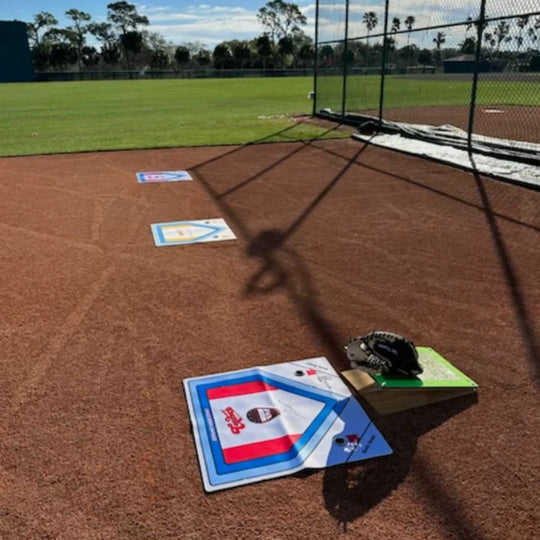 Baseball practice area with a catcher's mat, mitt and training device on a dirt field.